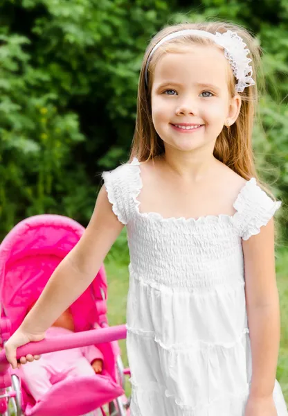 Menina bonito com sua carruagem de brinquedo e boneca — Fotografia de Stock