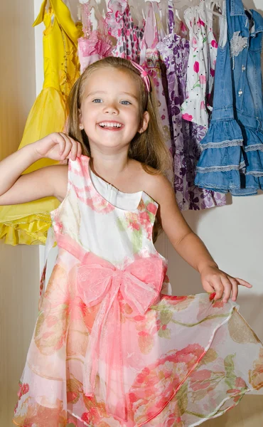 Schattig lachende klein meisje kiest een jurk uit de kast — Stockfoto