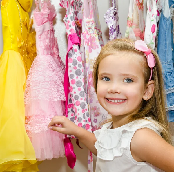 Leende liten flicka väljer en klänning från garderoben — Stockfoto