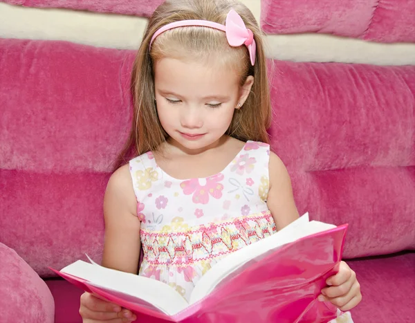 Kleines Mädchen liest ein Buch und sitzt auf dem Sofa — Stockfoto