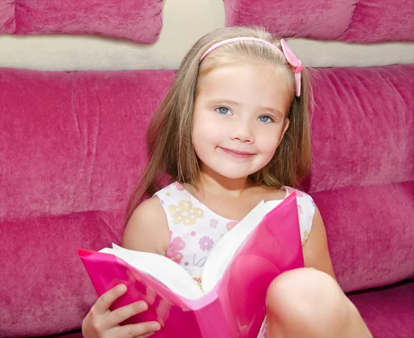 Kleines Mädchen liest ein Buch und sitzt auf dem Sofa — Stockfoto