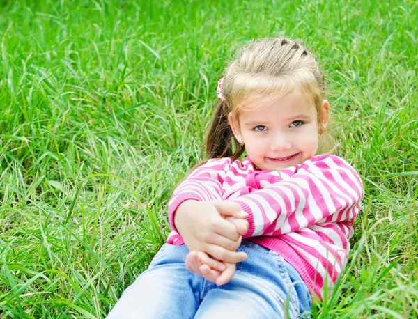 Милая улыбающаяся маленькая девочка, лежащая в траве на лугу — стоковое фото