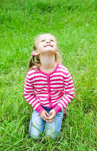 Linda niña sonriente tendida en la hierba en el prado — Foto de Stock