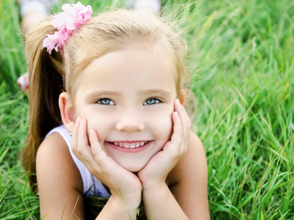 Carino sorridente bambina sdraiata in erba sul prato — Foto Stock