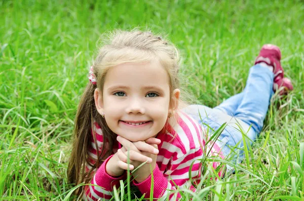 Söt leende liten flicka liggande i gräset på ängen — Stockfoto