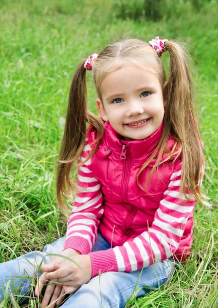Мила усміхнена маленька дівчинка лежить у траві на лузі — стокове фото