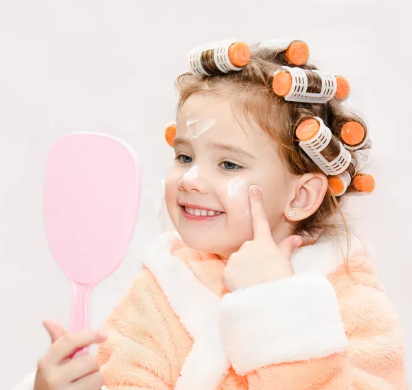 Happy cute little girl in hair curlers with mirror applying crea — Stock Photo, Image