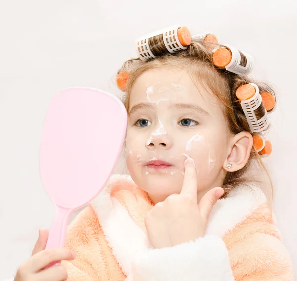Cute little girl in hair curlers with mirror applying cream isol — Stock Photo, Image