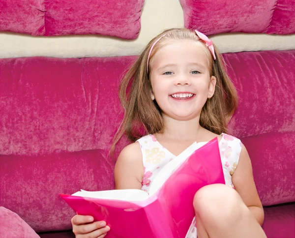 Nettes kleines Mädchen liest ein Buch und sitzt auf dem Sofa — Stockfoto