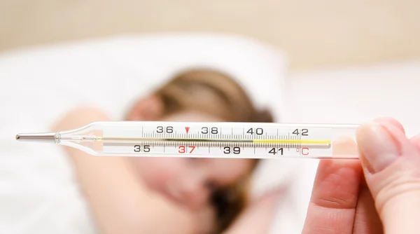 Mother holding thermometer foreground and sick little girl — Stock Photo, Image