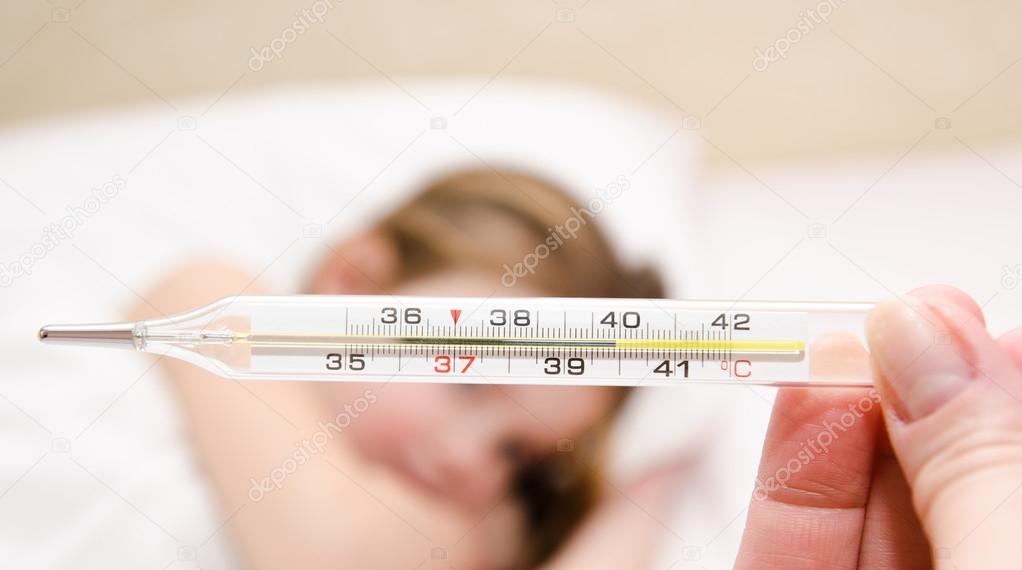Mother holding thermometer foreground and sick little girl
