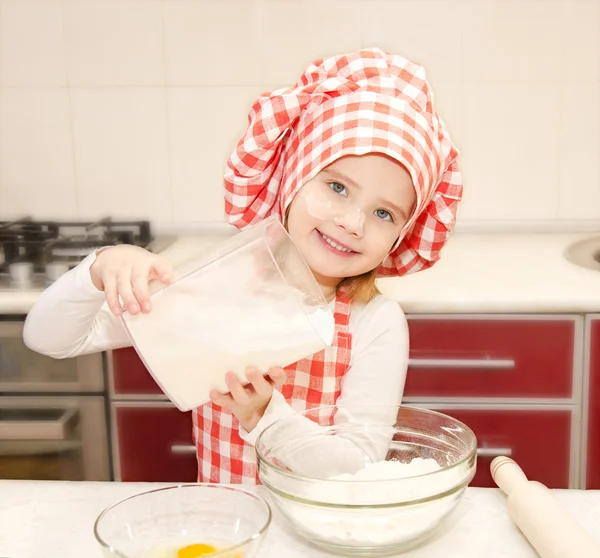 Smilende lille pige med kok hat sætte mel til bagning cookies - Stock-foto