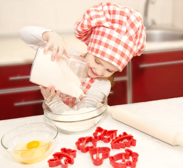 Ragazzina sorridente con cappello da chef mettere la farina per i biscotti di cottura — Foto Stock