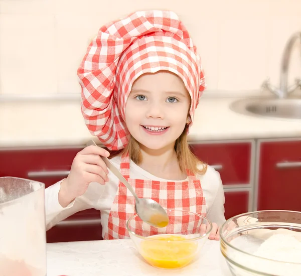 Chef şapka stirrring kurabiye hamuru ile küçük kız gülümseyerek — Stok fotoğraf