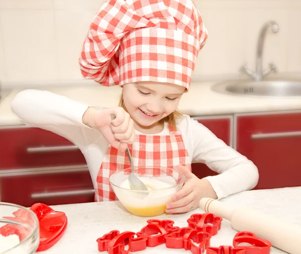 Chef şapka stirrring kurabiye hamuru ile küçük kız gülümseyerek — Stok fotoğraf