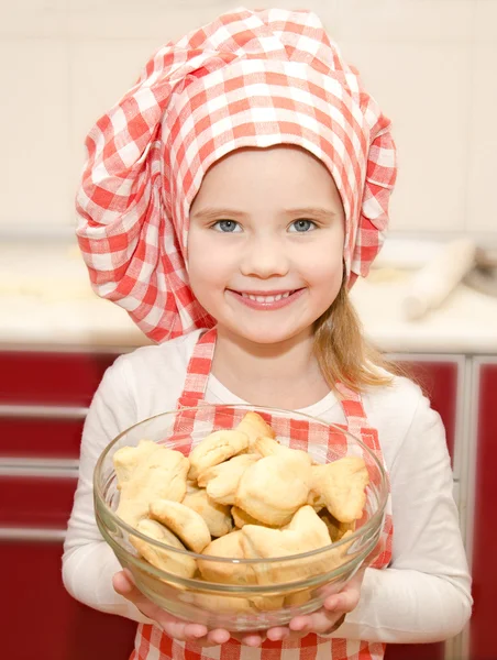 Leende liten flicka i kock hat håller skål med cookies — Stockfoto