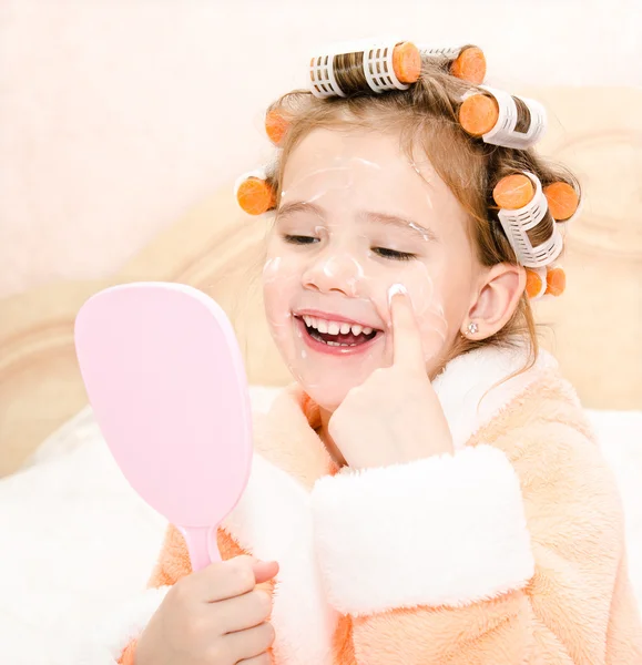 Happy cute little girl in hair curlers with mirror applying crea — Stock Photo, Image
