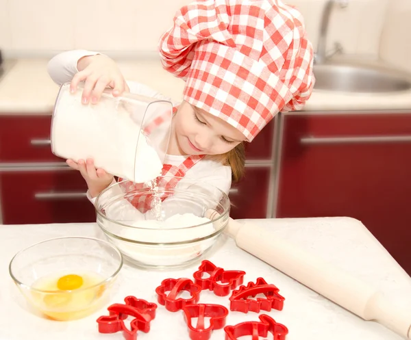 Liten flicka med kock hat lägga mjöl för bakning cookies — Stockfoto