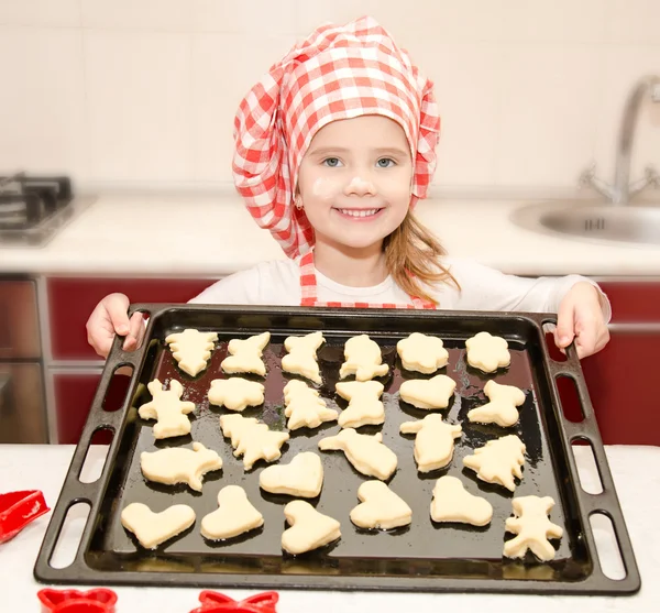 Leende liten flicka i kocken hatt med plåt av cookies — Stockfoto