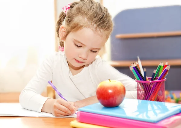 La niña está escribiendo en el escritorio en preescolar. — Foto de Stock