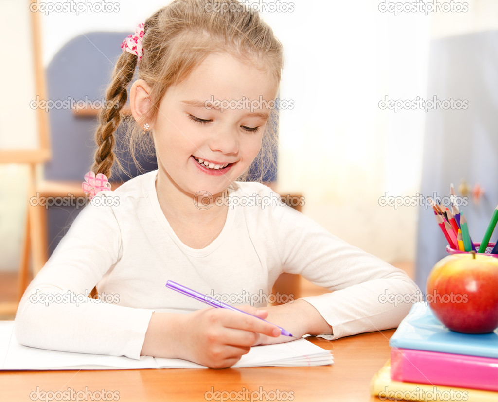 Cute little girl is writing at the desk  in preschool