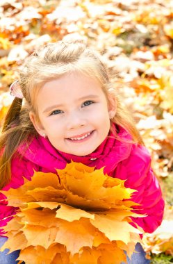 Sonbaharda akçaağaç yaprakları ile gülümseyen sevimli küçük kız portresi