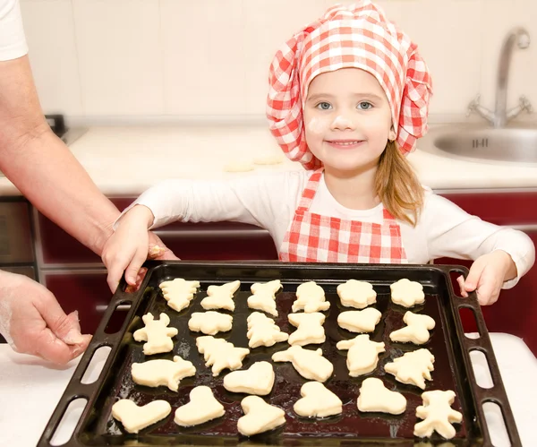 Ragazzina sorridente in cappello da chef con teglia di biscotti — Foto Stock