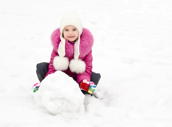 Cute smiling little girl makes snowman in winter day — Stock Photo, Image