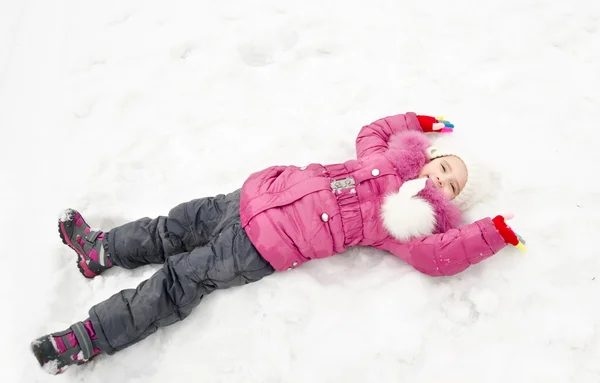 Cute smiling little girl lying on snow in winter day — Stock Photo, Image