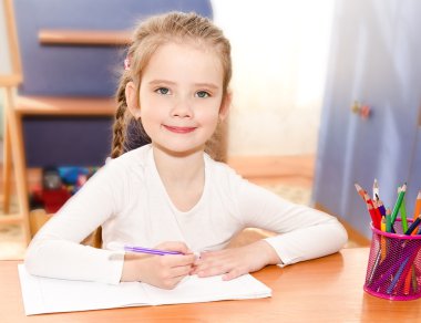 Cute smiling little girl is writing at the desk  clipart