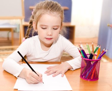 Cute little girl is writing at the desk clipart