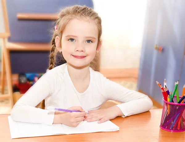 Carino sorridente bambina sta scrivendo alla scrivania — Foto Stock