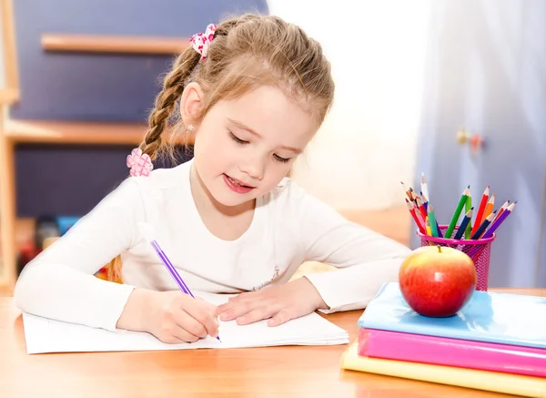 Carino sorridente bambina sta scrivendo alla scrivania — Foto Stock