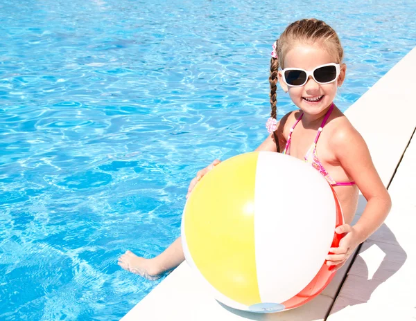 Улыбающаяся маленькая девочка с мячом в бассейне — стоковое фото