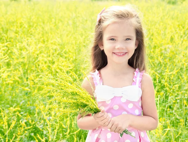 Bedårande leende liten flicka med gula blommor på ängen — Stockfoto