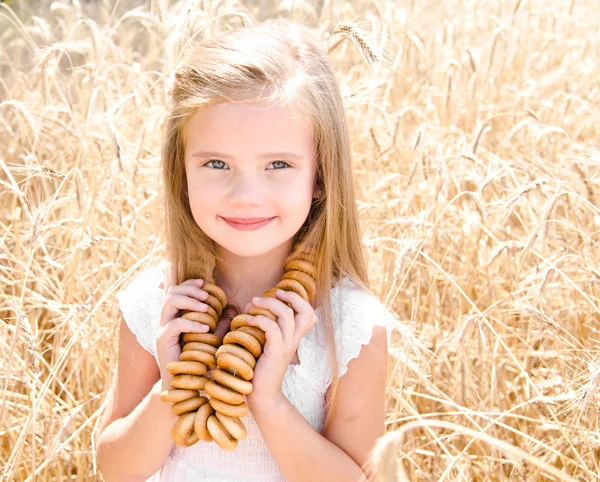 Smiling little girl on field of wheat with bagels — Stock Photo, Image