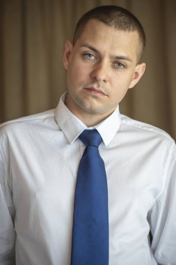 Beyaz gömlekli ve mavi kravatlı genç bir adamın portresi.