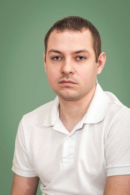 Yeşil arka planda beyaz tişörtlü genç bir adamın portresi.