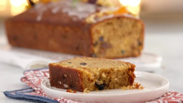 La mano femenina rompe un trozo de un bifurcador en rodajas de pastel de frutas. Ambiente navideño con linternas al fondo. Pastelito casero de Navidad. Panecillo tradicional con frutas secas para Navidad. — Vídeos de Stock