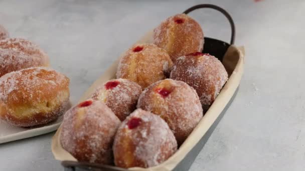 Berlineses. Las manos femeninas ponen las rosquillas con la confitura de frambuesa en la bandeja de servir sobre el fondo blanco, la rosquilla con el relleno que gotea. Deliciosas rosquillas dulces. Hacer rosquillas con mermelada. — Vídeos de Stock