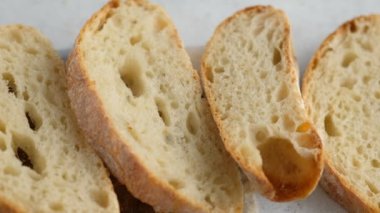 Kamera hareketi. Üst Manzara. Dilimlenmiş ekmek tahta bir tahtanın üzerinde yatıyor. Ekmek pişiriyorum. Ciabatta pişiriyorum. İtalyan ekmeği.