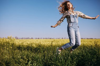 Neşe dolu genç bir kadın çiçek tarlasının ortasına atlıyor ve güneşin tadını çıkarıyor.