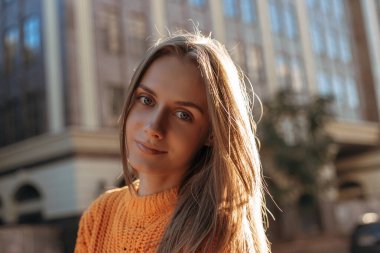 Şehir sokaklarında gülümseyen sarı saçlı genç bir kadının portresi. Gün batımında kamerada poz veren kadın model.