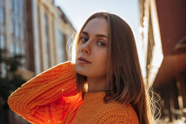 日没の建物の背景に若いブロンドの女性の肖像画 赤いニットのセーターを着た女の子がカメラをポーズ ロイヤリティフリーのストック画像