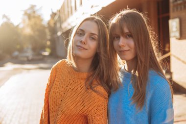 Uzun sarı saçlı güzel ikiz kardeş kameraya bakıyor ve gülümsüyor.