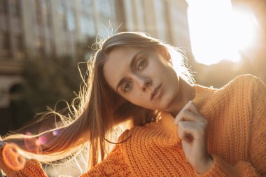 Sarışın kadın saçlarını uzatıyor. Kadın model kameraya bakıyor ve şehir caddesinde poz veriyor. Yakın plan portre