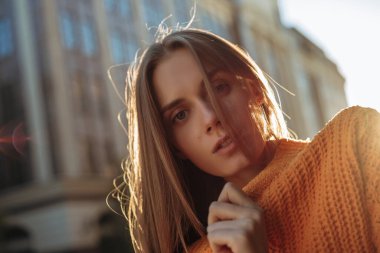 Şehir sokaklarında gülümseyen sarı saçlı genç bir kadının portresi. Gün batımında kamerada poz veren kadın model.