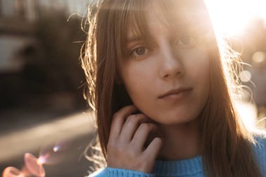 Cute and positive young blonde woman looking at camera and touching her neck