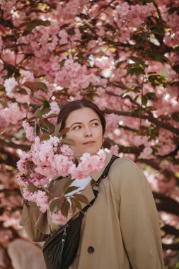 Japon Sacura ağacının çiçek açan dallarıyla poz veren romantik bir kadın model.