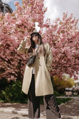 trendy young caucasian white woman standing on the sacura tree background. Low angle view